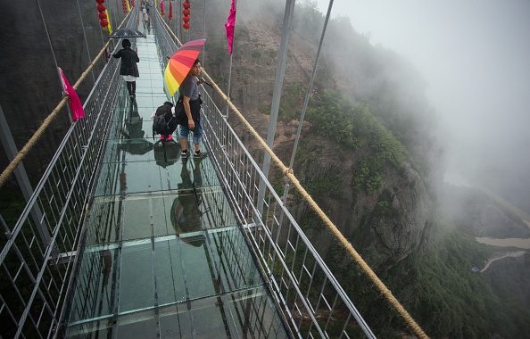 Chinese tourists walk across a glass-bottomed suspension bridge in the Shinuizhai mountains in Pingjang county, Hunan province some 150 kilometers from Changsha on October 7, 2015. The bridge, originally a wooden walkway spanning some 300 meters across the 180-meter deep valley, reopened two weeks ago following renovations as a glass-bottomed tourist attraction.