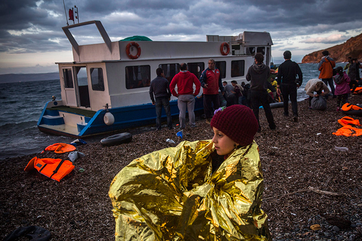 A girl tries to warm up on a beach with a thermal blanket after arriving with around 125 people from the Turkish coast to the northeastern Greek island of Lesbos, Thursday, Oct. 29, 2015.