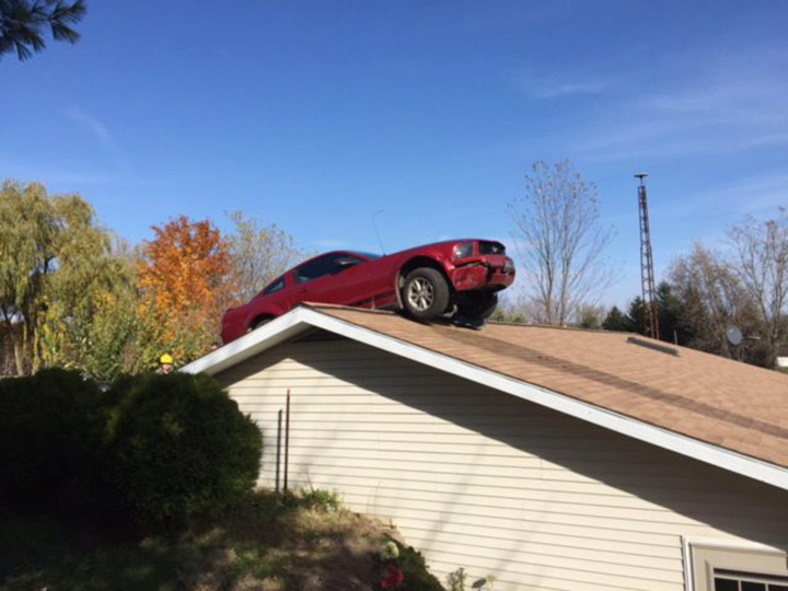 In this Oct. 26, 2015 photo provided by the Michigan State Police, a Ford Mustang sits on a roof of a house in Woodhull Township, Mich. State police say the driver had a medical problem and lost control of his car on Interstate 69 in Shiawassee County. 
