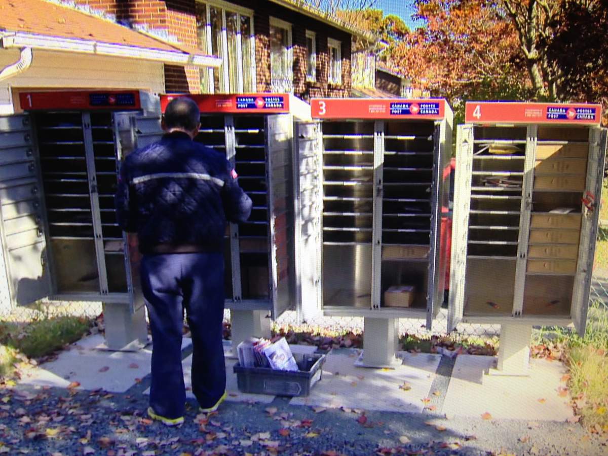 A letter carrier puts mail in a community mailbox. 
