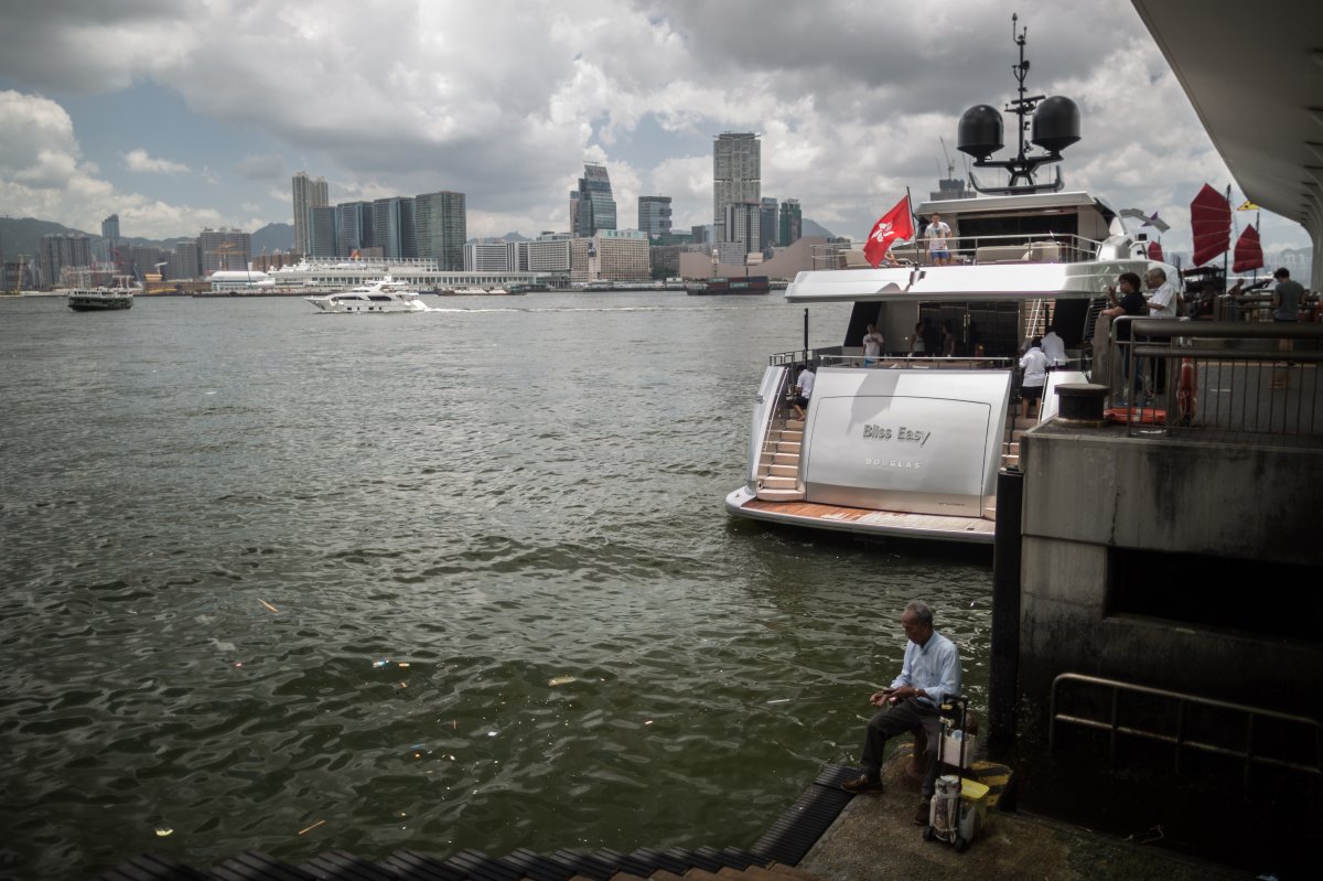 An elderly man line fishes on the steps of a pier near Hong Kong's Victoria Harbour as passengers board a luxury yacht.