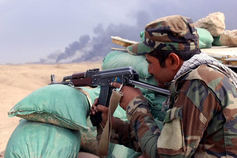 An Iraqi soldier aims his gun as smoke rises from the Ajeel oil field during the clashes between the fighters of jihadist Islamic State and Iraqi forces near Baiji city, northern Iraq, 22 October 2015.