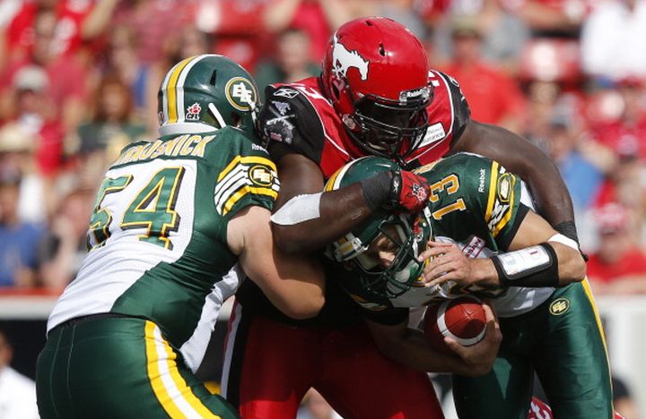 Quarterback Mike Reilly #13 of the Edmonton Eskimos is sacked by Cordarro Law #49 Calgary Stampeders while Alexander Krausnick #54 tries to block the tackle in the first half of their CFL football game September 2, 2013 in Calgary, Alberta, Canada. 