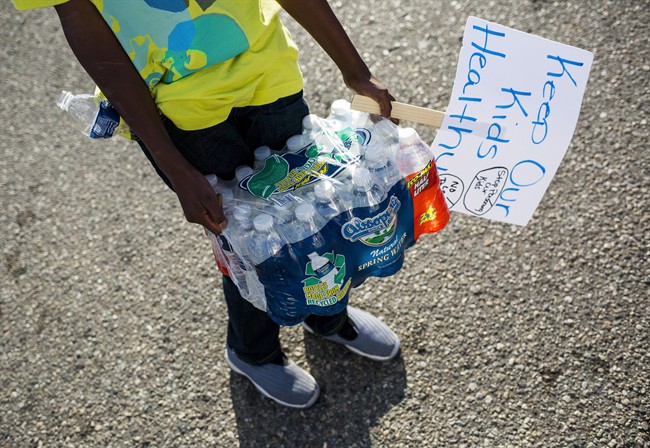 Community leaders pass out cases of bottled water to Flint residents on Wednesday, Oct. 7, 2015, in downtown Flint, Mich. The head of Michigan's health department has been charged with involuntary manslaughter over the water crisis.