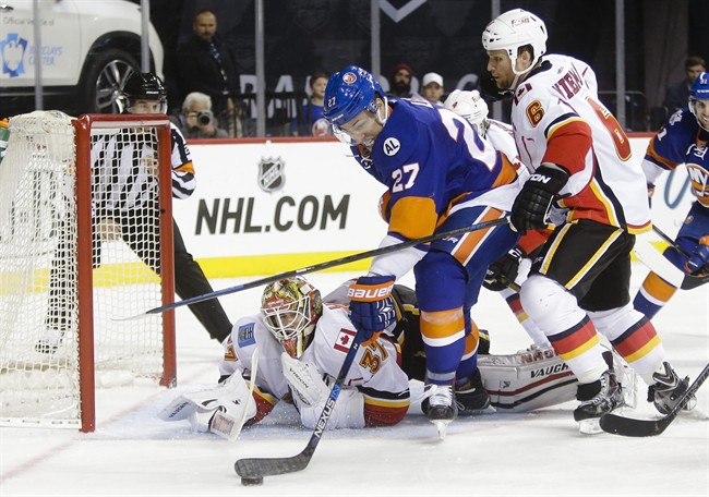 Calgary Flames goalie Joni Ortio (37) and Dennis Wideman (6) defend New York Islanders' Anders Lee (27) during the second period of an NHL hockey game Monday, Oct. 26, 2015, in New York.