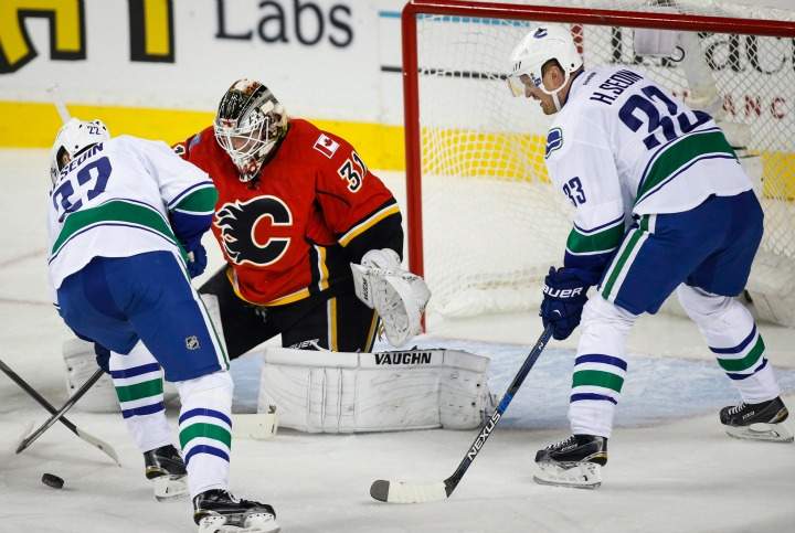 Vancouver Canucks' Daniel Sedin, left, from Sweden, tries to get the puck to his brother Henrik Sedin, right, as Calgary Flames goalie Karri Ramo, from Finland, looks on during first period NHL hockey action in Calgary, Wednesday, Oct. 7, 2015.