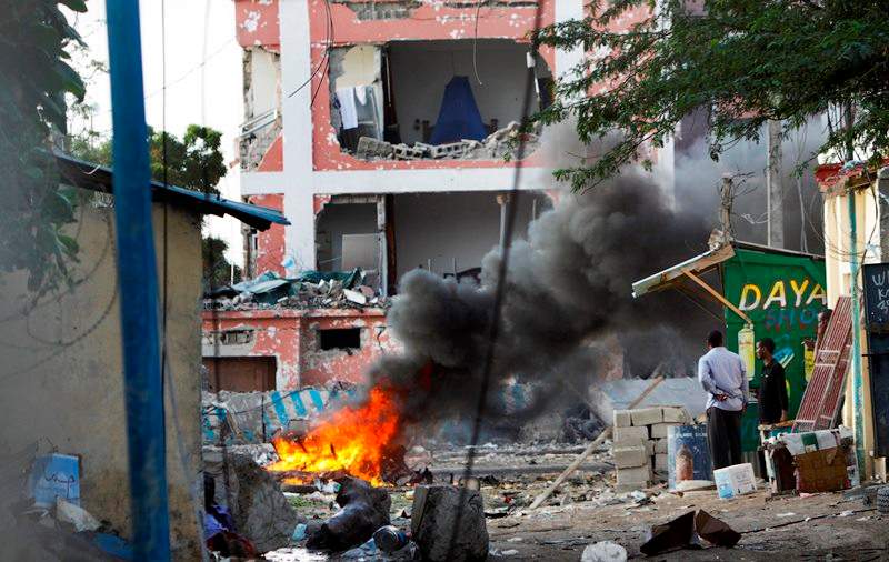 Somali men watch as fires burn amidst the destruction outside the Sahafi Hotel in Mogadishu, Somalia Sunday, Nov. 1, 2015.