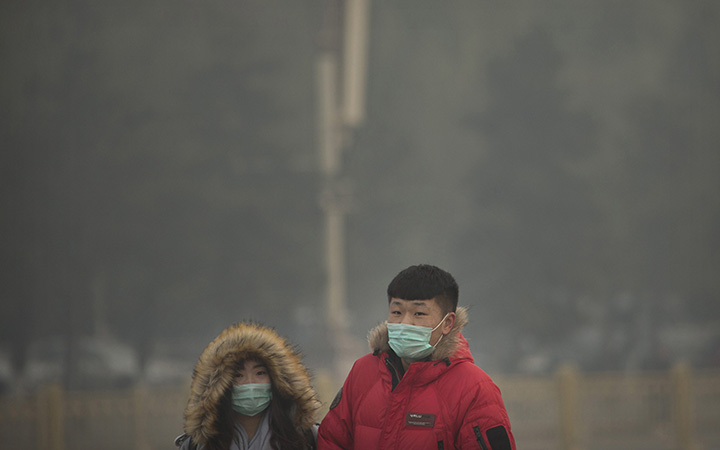 People wearing face masks walk across Tiananmen Square on a day with poor air quality in Beijing, Saturday, Nov. 28, 2015. 