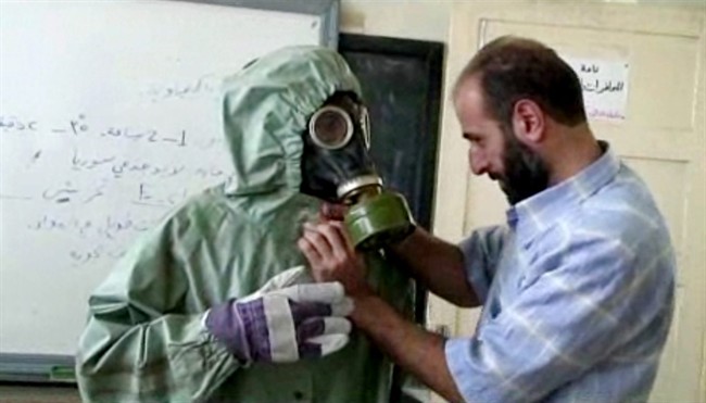 This image made from an AP video posted on Wednesday, Sept. 18, 2013 shows a volunteer adjusting a students gas mask and protective suit during a session on reacting to a chemical weapons attack, in Aleppo, Syria. Russia and China have blocked a UN resolution that would have imposed sanctions on 21 Syrian individuals, organizations and companies allegedly involved in chemical weapons attacks.