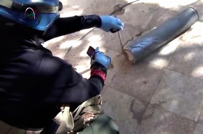 In this August 26, 2013, file image taken from amateur video posted online, appears to show a presumed UN staff member measuring and photographing a canister in the suburb of Moadamiyeh in Damascus, Syria.