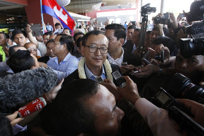 In this Sunday, Aug. 16, 2015, photo, Sam Rainsy, center, leader of the opposition Cambodia National Rescue Party (CNRP), talks to journalists upon his arrival at Phnom Penh International Airport in Phnom Penh, Cambodia.