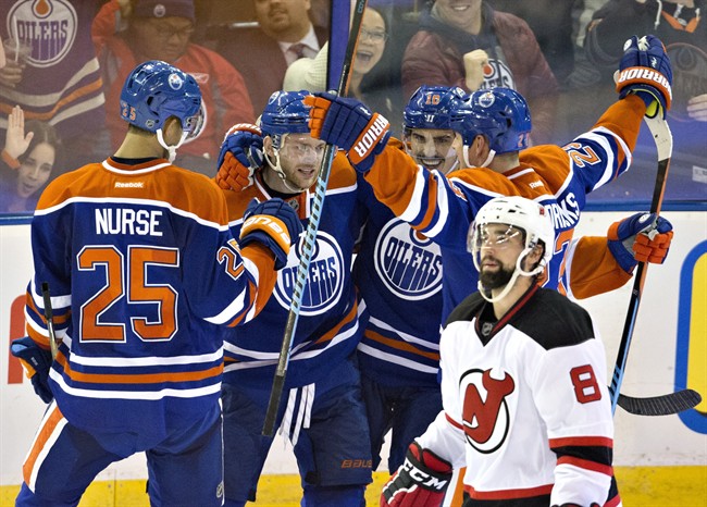 New Jersey Devils' David Schlemko (8) skates past as the Edmonton Oilers celebrate a goal during third period NHL action in Edmonton, Alta., on Friday November 20, 2015.