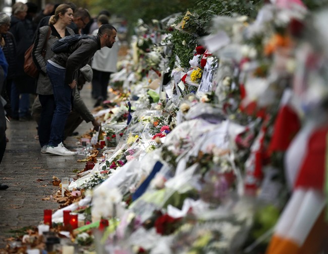 People look at flowers and card tributes placed outside the Bataclan concert hall in Paris, Thursday, Nov. 19, 2015.