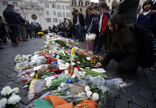 People gather in front of flowers that were laid outside the French embassy in Rome, Saturday, Nov. 14, 2015. French police on Saturday hunted possible accomplices of eight assailants who terrorized Paris concert-goers, cafe diners and soccer fans with a coordinated string of suicide bombings and shootings in France's deadliest peacetime attacks. (AP Photo/Gregorio Borgia).