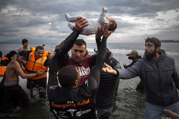 A volunteer holds up a baby as others help migrants and refugees to disembark from a dinghy after their arrival from the Turkish coast to the Greek island of Lesbos, Wednesday, Nov. 25, 2015.