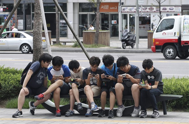 South Korean high school students play games on their smartphones on a bench on the sidewalk in Seoul, South Korea.
