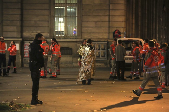People wearing survival blanket stand near Rue de Charonne, one of the sites targetted in Friday's shootings, in Paris, Saturday, Nov. 14, 2015.