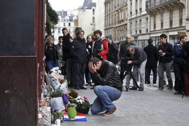 A man holds his head in his hands as he lays flowers in front of the Carillon cafe, in Paris, Saturday, Nov.14, 2015. French President Francois Hollande vowed to attack Islamic State without mercy as the jihadist group admitted responsibility Saturday for orchestrating the deadliest attacks inflicted on France since World War II. (