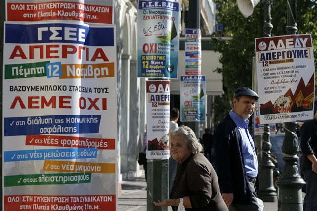 An elderly woman begs next to banners announcing tomorrow's general strike in Athens, Wednesday, Nov. 11, 2015.