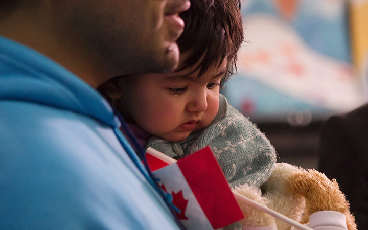 A young Syrian refugee is held by her father as they arrive at the Welcome Centre at Toronto's Pearson Airport on Friday December 18, 2015. 