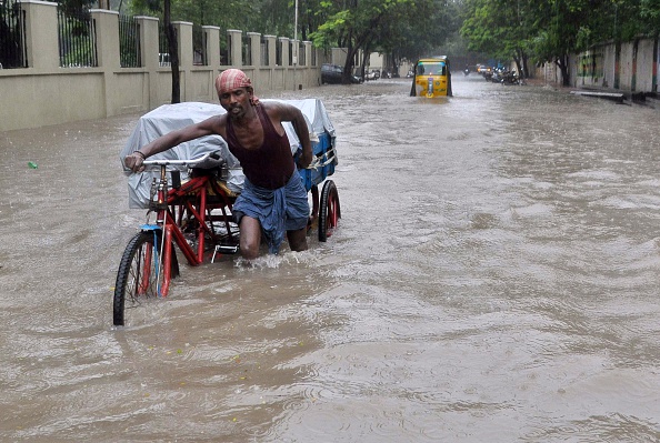 An Indian labourer pushes his cycle trishaw through floodwaters in Chennai on December 1, 2015, during a downpour of heavy rain in the southern Indian city.  Heavy rains pounded several parts of the southern Indian state of Tamil Nadu and inundating most areas of Chennai, severely disrupting flights, train and bus services and forcing the postponment of half-yearly school exams. 