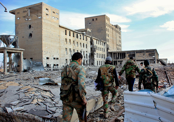 Syrian army soldiers patrol near a building previously used for storing seeds in the countryside of Deir Hafer, a former bastion of Islamic State group, near the northern Syrian city of Aleppo on December 2, 2015.
