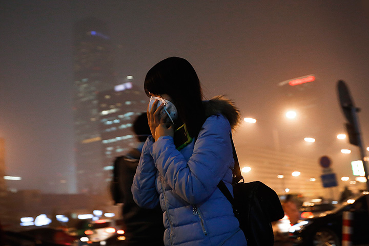A woman covers her face as she rushes to a subway station on a heavily polluted day in Beijing Tuesday, Dec. 8, 2015. 