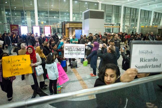 Members of groups who are sponsoring two Syrian refugee families hold up signs welcoming their charges as they wait for the families to arrive at Toronto\’s Pearson Airport, on Wednesday, Dec. 9, 2015.