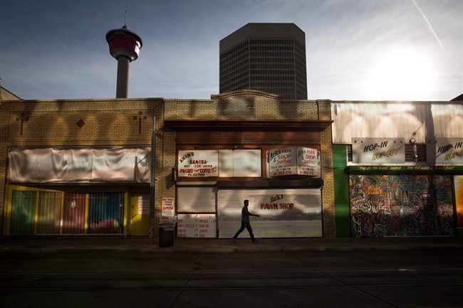 A man is silhouetted as sunlight reflects off the windows of an office tower onto another building in downtown Calgary on Sunday, October 18, 2015. 