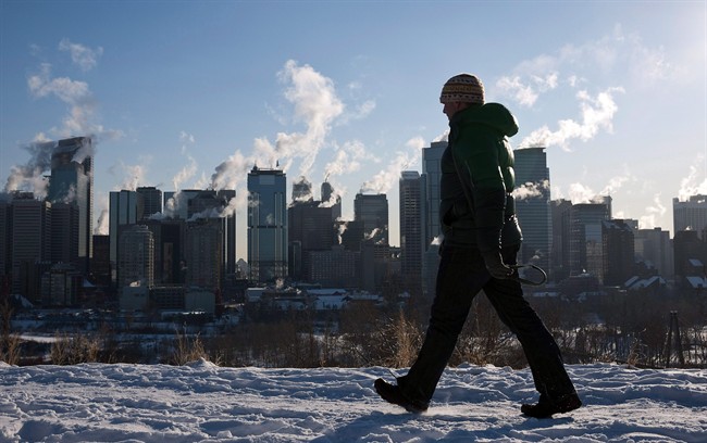 A man walks past the Calgary, Alta., skyline as steam rises from downtown office towers on Jan. 31, 2011. 