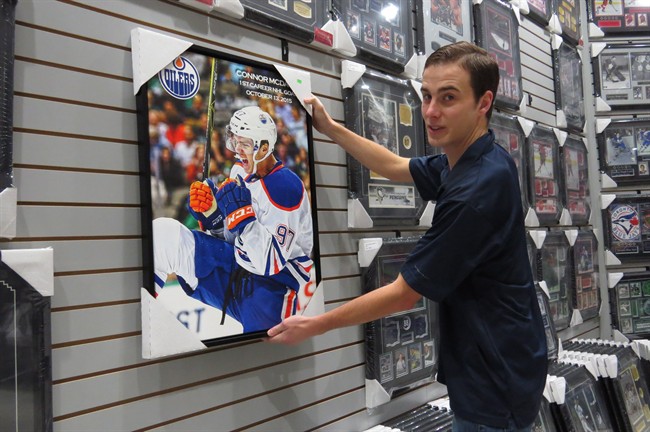 Jordan Forsythe, manager at West Edmonton Coin and Stamp, hangs up a Connor McDavid print for sale in Edmonton on Dec. 14, 2015. McDavid memorabilia has been the top seller since the teen from Newmarket, Ont., was drafted by the Oilers this summer, part of a McDavid led resurgence of hockey interest in the Alberta capital.