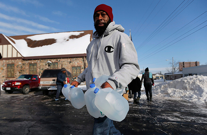 In this February 3, 2015 file photo, Lemott Thomas carries free water being distributed at the Lincoln Park United Methodist Church in Flint, Mich. Flint's mayor has declared a state of emergency due to problems with the city's water system caused by using water from the Flint River, saying the city needs more federal help. 