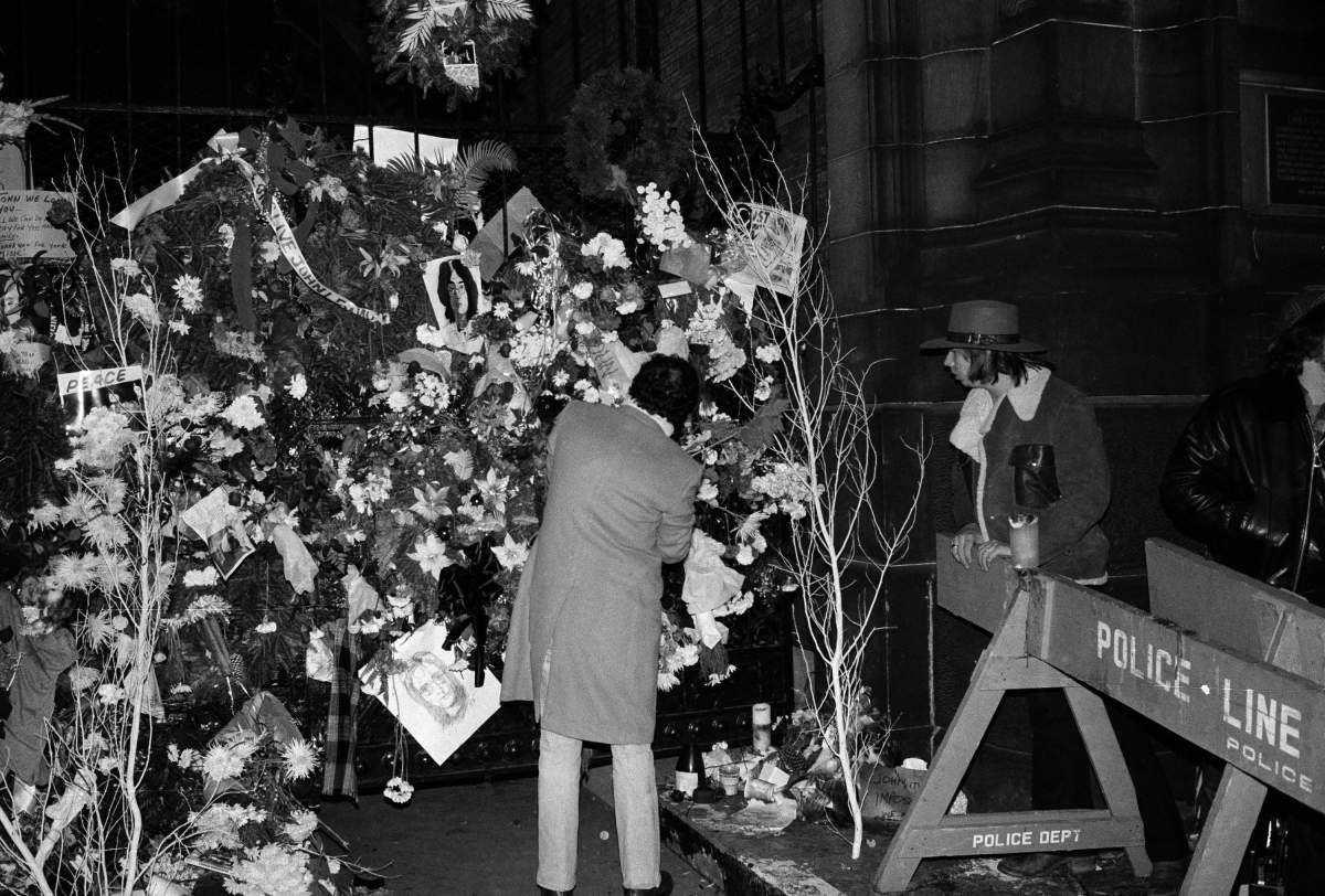 FILE – In this Dec. 10, 1980 file photo, a man adjusts one of the wreaths that cover the wrought iron front gate to the Dakota apartment building where John Lennon lived. Thirty-five years ago on Dec. 8, Mark David Chapman shot and killed Lennon with a gun he purchased legally in Hawaii, a former Beatles member. (AP Photo/Lyndon Fox, File)