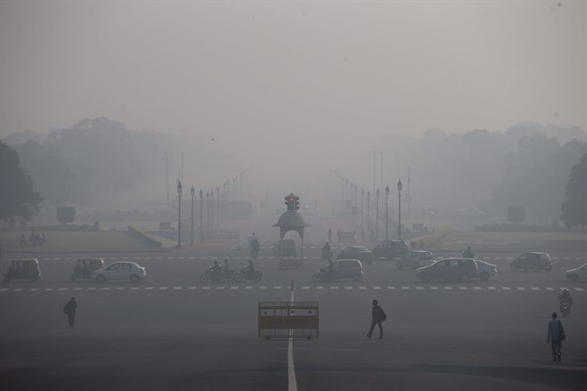 In this Nov. 24, 2015 photo, commuters walk as vehicles move at a traffic signal in New Delhi, India. Over the last decade the city's air pollution has grown so rapidly that the cold weather turns the city into a grey, smog-filled health nightmare. New Delhi has earned the dubious distinction of being the world's dirtiest city, surpassing Beijing, once the poster child for air pollution. (AP Photo /Tsering Topgyal).