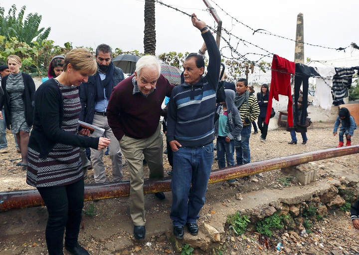Canadian Minister of Immigration John McCallum passes under barbed wire during his visit to a Syrian refugee camp in the southern town of Ghaziyeh, near the port city of Sidon, Lebanon, Friday, Dec. 18, 2015.