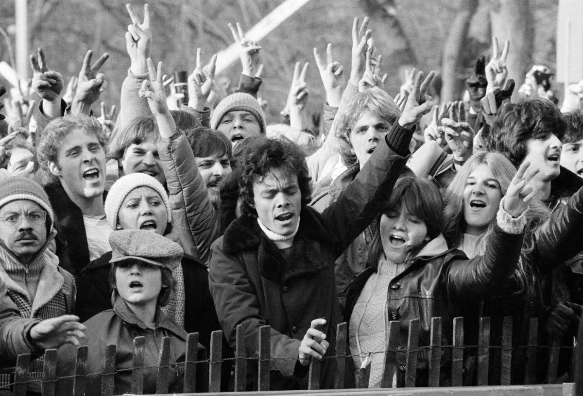 FILE – In this Dec. 14, 1980, file photo, people participating in tribute to the slain musician John Lennon wave the peace sign and sing “Give Peace A Chance” at New York’s Central Park. Thirty-five years ago on Dec. 8, Mark David Chapman shot and killed Lennon, a former Beatles member. (AP Photo/Carlos Rene Perez, File)