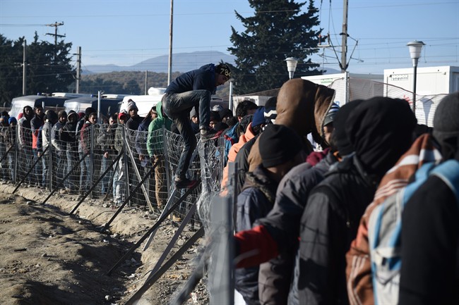 People wait to receive food provided by charities as a man climbs a fence at a refugee camp, near the northern Greek village of Idomeni, Tuesday, Dec. 8, 2015. 