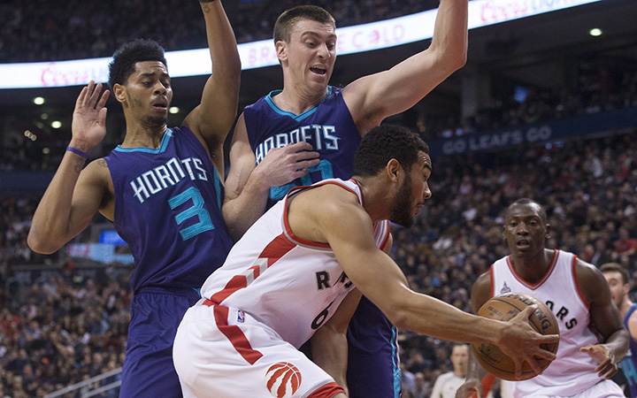 Toronto Raptors' Corey Joseph, centre, sets up a pass to Bismack Biyombo as he drives past Charlotte Hornets' Jeremy Lamb, left, and Tyler Hansbrough during first half NBA basketball action in Toronto on Friday January 1, 2016. 