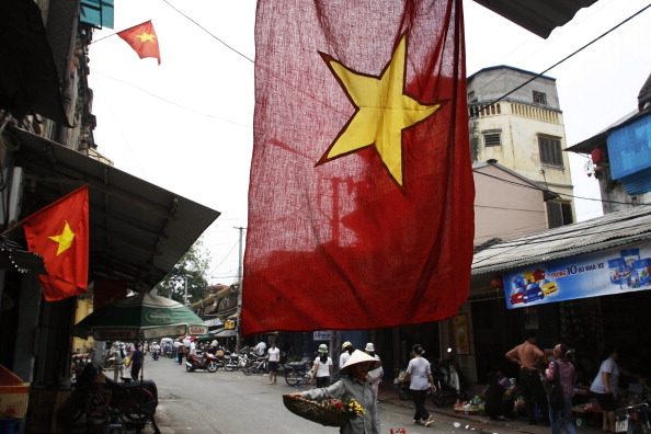 A national flag hangs outside a home in Hanoi as a street vendor walks by. (Photo by Yvan Cohen/LightRocket via Getty Images).