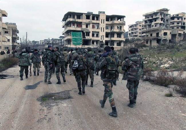 In this photo released on Tuesday, Jan 12, 2016, by the Syrian official news agency SANA, shows Syrian government troops and allied militiamen walk inside the key town of Salma in Latakia province, Syria.