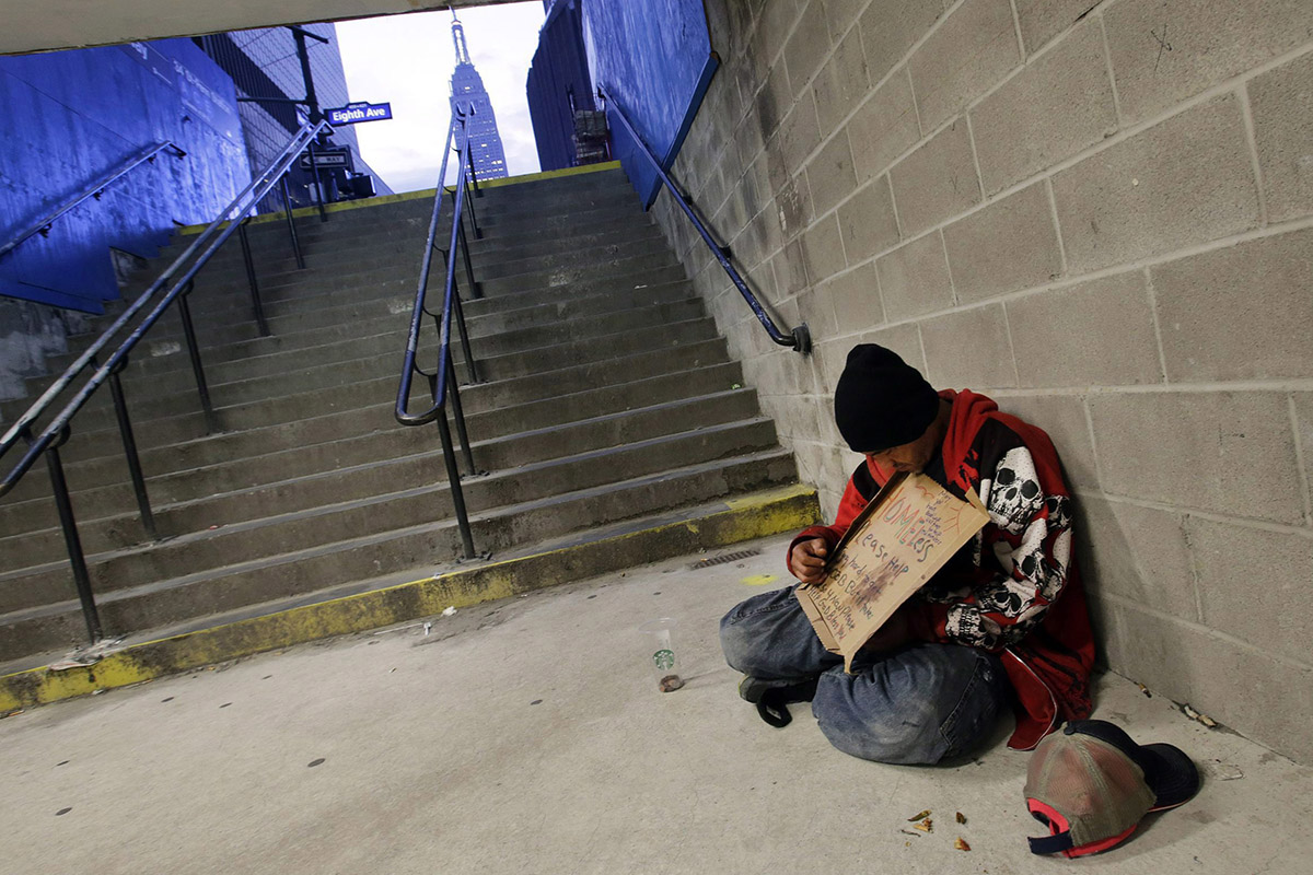  In this file photo, a homeless man holds a sign asking for money while sitting at the entrance to a subway station in New York. 