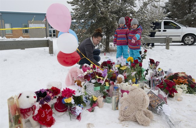 Tashina Montgrand lays flowers outside the La Loche Community School as her daughters Tayala and Tayvah look on in La Loche, Sask.