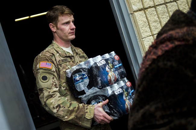Michigan National Guard Staff Sgt. Stephen Robel helps carry a case of water to the vehicle of Flint resident Karand Houston.