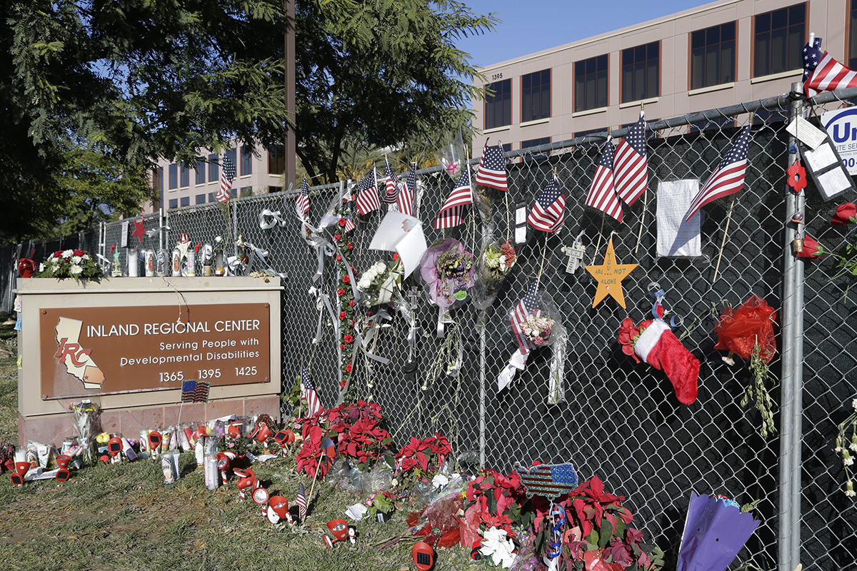 In this Tuesday, Dec. 29, 2015, photo, flowers and American flags honoring the victims of the attack on Dec. 2 are placed outside the Inland Regional Center where the fatal shooting took place in San Bernardino, Calif.