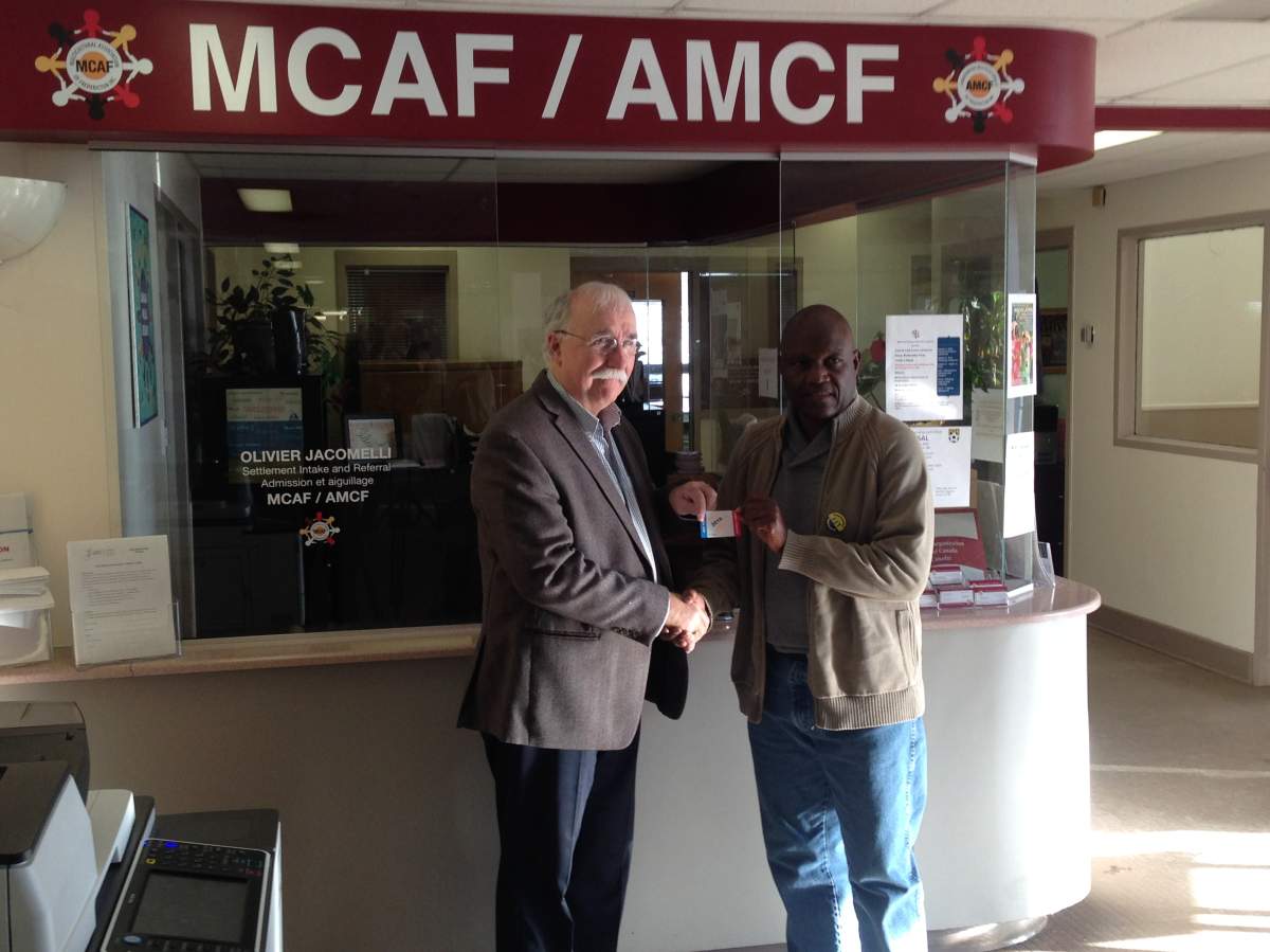 Deputy Mayor Eric Megarity presents a member of the Multi-Cultural Association with a Fredericton transit pass. 