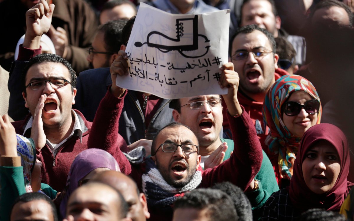 Egyptian doctors shout anti-police slogans as one holds a banner showing a police boot stepping on a medical stethoscope with Arabic slogan reading, "police are thugs," during a protest against rampant police abuses, after two doctors were beaten up by policemen in a Cairo hospital, in front of their headquarters of the Egyptian Medical Syndicate in Cairo, Egypt, Friday, Feb. 12, 2016. 