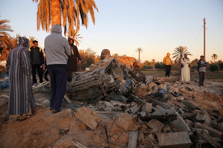 In this Friday, Feb. 19, 2016 photo, people gather after an air strike on a house and training camp belonging to the Islamic State group, west of Sabratha, Libya. 