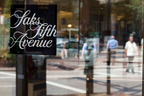 Pedestrians are reflected in the glass doors of a Saks Fifth Avenue store .