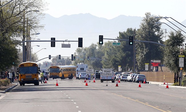 Buses make their way to bring parents waiting to reunite with their children, Friday, Feb. 12, 2016, in Glendale, Ariz. after two teens were shot in an apparent murder-suicide at Independence High School in the Phoenix suburb. 