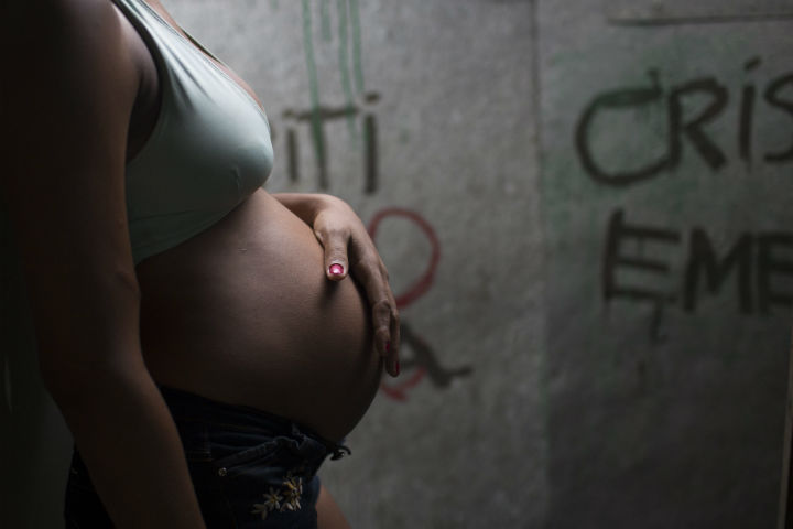 In this Jan. 29, 2016 photo, Tainara Lourenco stands in the entrance of her stilt home with her hand on her baby bump, at a slum in Recife, Brazil. Unemployed and five months pregnant, 21-year-old Lourenco lives in a slum at the epicenter of Brazil’s tandem Zika and microcephaly outbreaks, in the state of Pernambuco. 